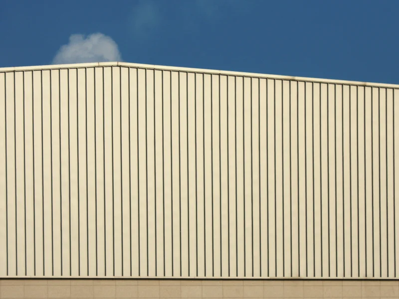 Fachada de galpón revestida con paneles metálicos verticales bajo cielo azul